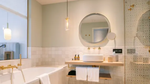 Elegant bathroom featuring a round mirror above a countertop with a sink, complemented by a bathtub and modern tiled walls.