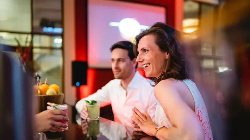 Eine Frau und ein Mann sitzen an einer Bar und trinken Cocktails.