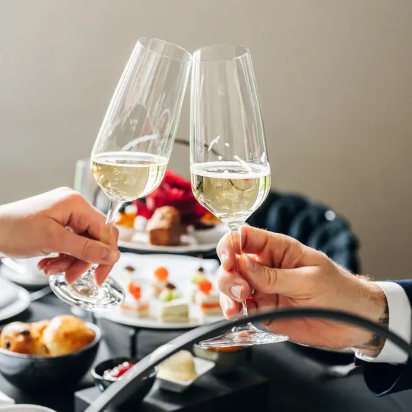 Two people clink their champagne glasses in front of a laid table. 