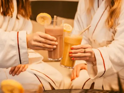 Zwei Frauen in Bademänteln halten Getränke in den Händen.