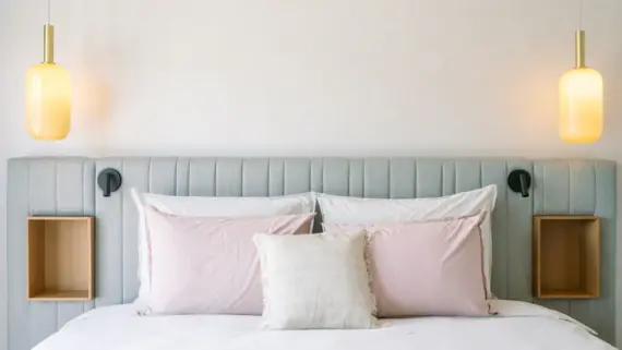 Cozy hotel bedroom featuring a neatly made bed with plush pillows and two elegant bedside lamps hanging from the ceiling.