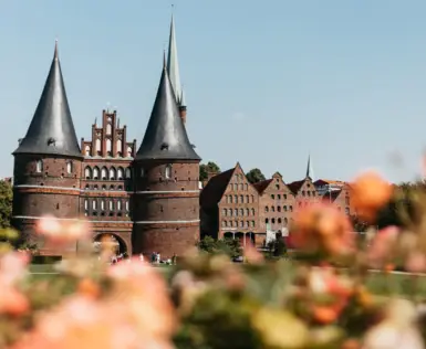 Das Holsten-Tor in Lübeck mit zwei Türmen und einer Rasenfläche mit Blumen im Vordergrund.