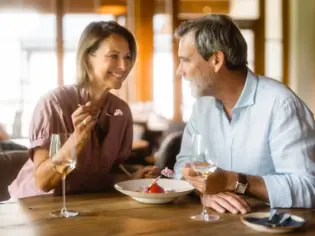 Ein Paar teilt sich lächelnd eine Portion Eiscreme in einem Restaurant und genießt dazu ein Glas Weißwein. 