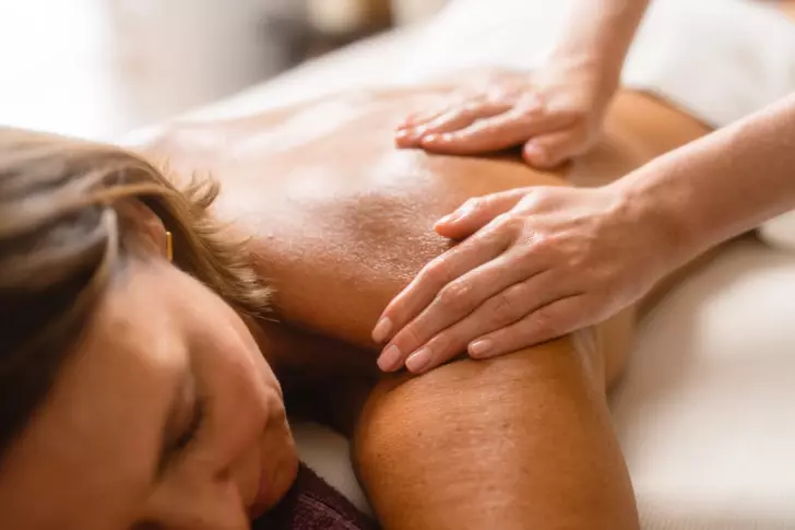A woman lying down indoors receiving a back massage.