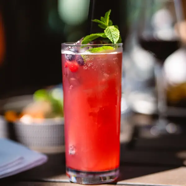 Ein Glas rotes Getränk mit Minzblättern und Strohhalm.