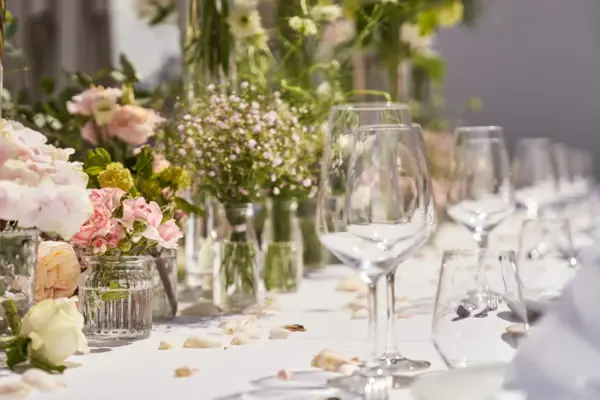 Ein elegant frisch gedeckter Hochzeitstisch, mit vielen grünen, weißen und rosafarbenen Blümchen in Glasvasen.