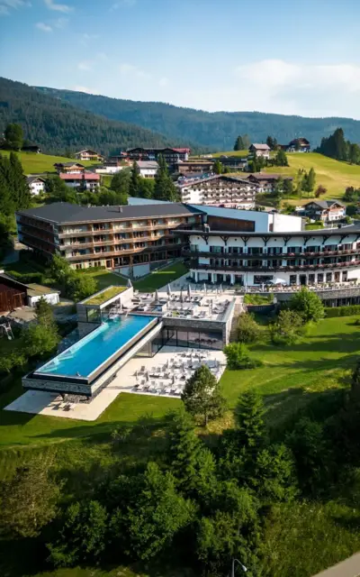 Ein Gebäude mit einem Infinity Pool inmitten eines Bergdorfs, umgeben von Bäumen und Grünflächen.