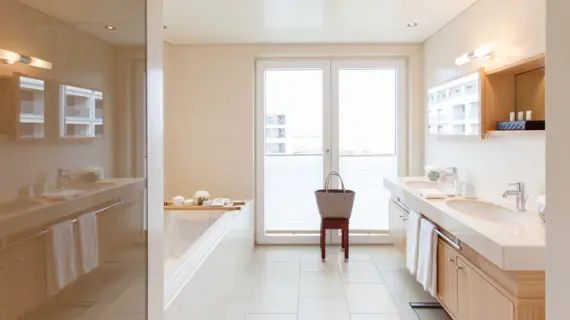 Ein helles modernes Badezimmer mit einem großem Waschtisch, einer Badewanne sowie einer Dusche.