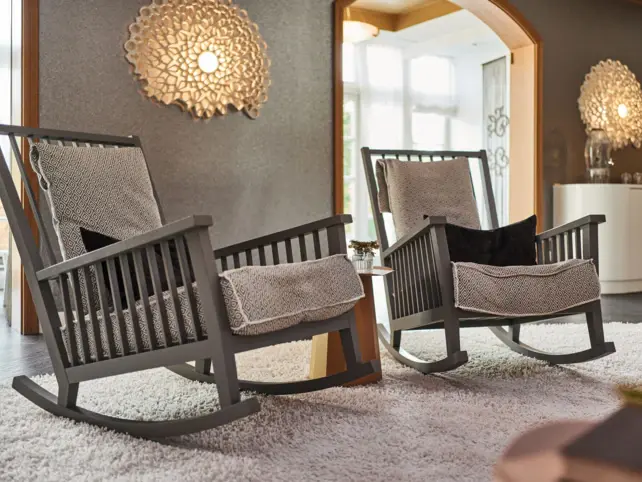 Two gray and comfortably upholstered rocking chairs stand in a warmly lit wellness area. 