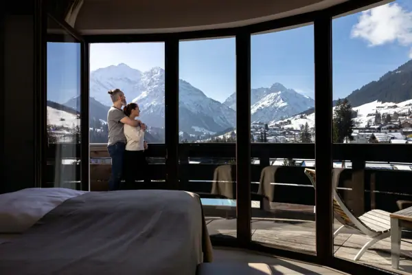 Ein Paar steht vor einem großen Fenster mit Blick auf eine verschneite Berglandschaft.