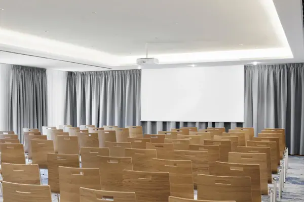 Ein Tagungsraum im A-ROSA Tegernsee mit Stuhlreihen und einem Beamer und einer Leinwand.