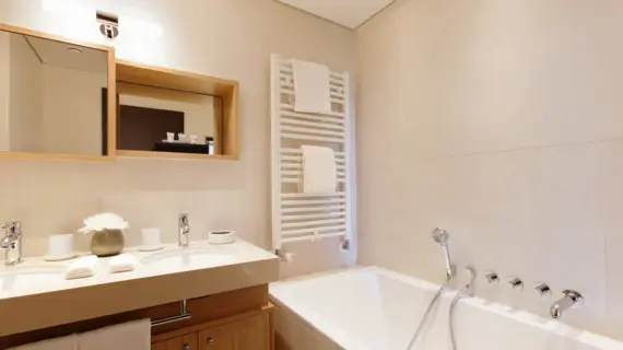 A bright bathroom with a bathtub and a vanity unit with two washbasins. There is a towel warmer above the bathtub.