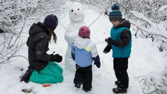 A woman builds a snowman with two children.