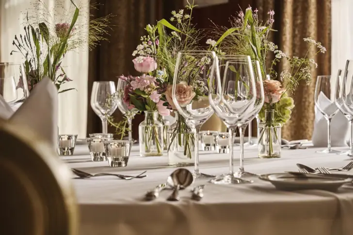 Elegant gedeckter Tisch mit Blumen und Kerzen als Mittelstück.