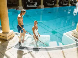 Ein Mann und eine Frau im Swimmingpool, umgeben von Wasser und blauem Himmel und Bergen im Hintergrund.