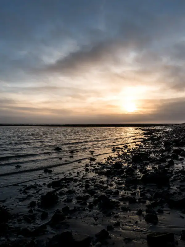Strand mit Felsen und Wasser bei ruhigem Himmel.