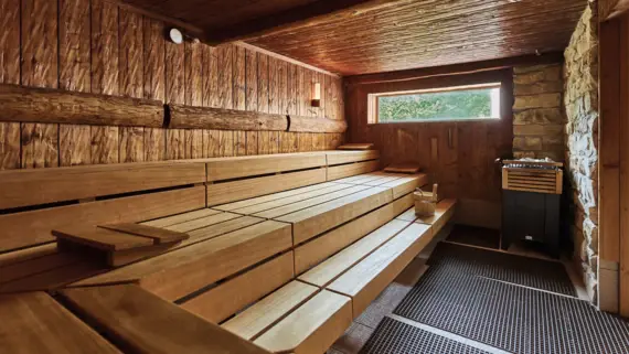 Holzbank in einer Sauna aus hellem Holz und mit einem kleinen Fenster.