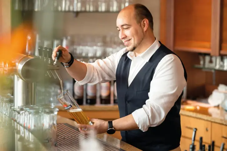 Mann zapft Bier aus einem Hahn in einer Bar.