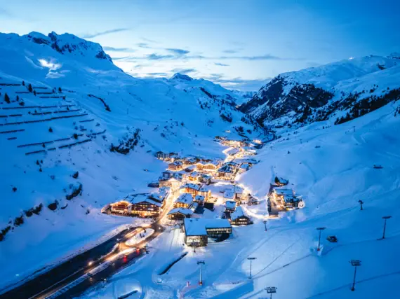 Eine Luftansicht eines kleinen von Licht beleuchteten Dorfes im Tal von schneebedeckten Bergen. 