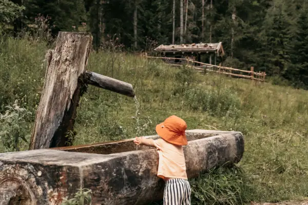 Ein Kind trinkt aus einem Trinkbrunnen im Freien.