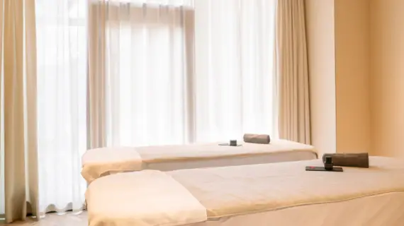 Two treatment beds in a stylishly furnished wellness room with light-colored curtains.