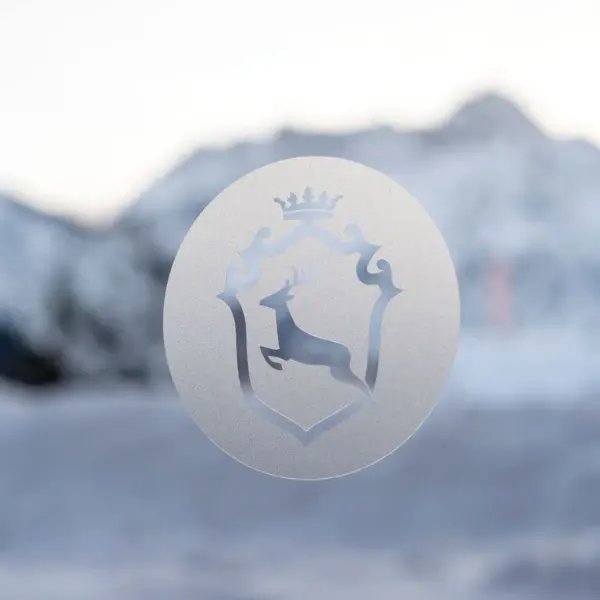 Logo des Ifen Hotel Kleinwalsertal in Folie auf einer Scheibe vor einer schneebedeckten Bergkulisse.