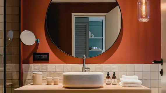 Modern bathroom featuring a round mirror above a sink, with tiled walls and a visible tap.