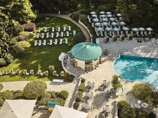 Swimming pool surrounded by chairs and lush greenery in an outdoor garden setting.