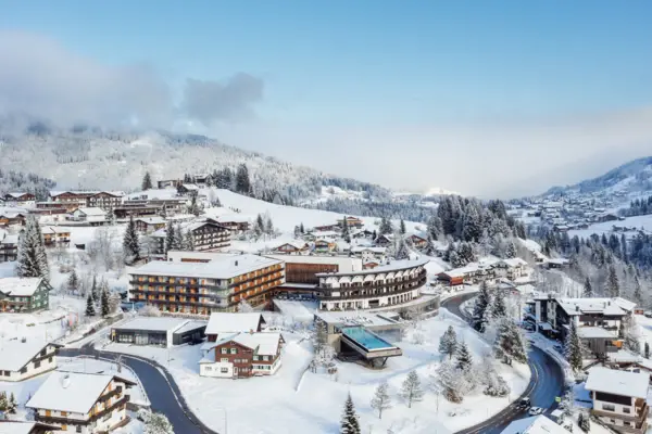 Gebäude mit einem Infinity-Pool inmitten eines Bergdorfes, umgeben von Bäumen und einer Landschaft mit Bergen.