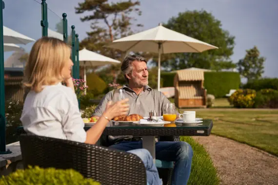 Ein Mann und eine Frau sitzen an einem gedeckten Frühstückstisch im Freien.