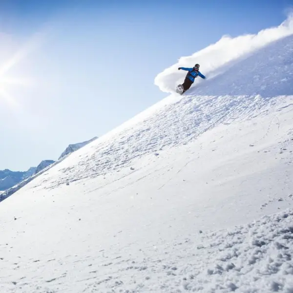 A snowboarder in blue clothing riding down a steep slope.