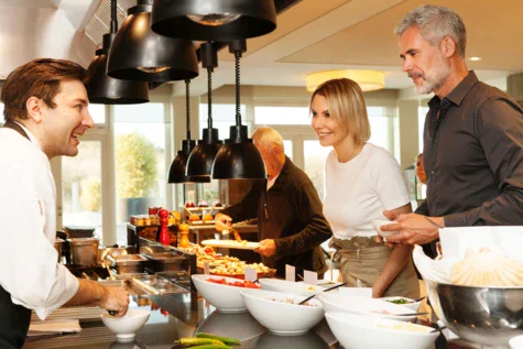 Gruppo di persone in piedi intorno a un buffet in un ambiente interno.