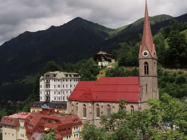 Eine Kirche auf einem Hügel, umgeben von Bergen und Bäumen unter einem bewölkten Himmel.