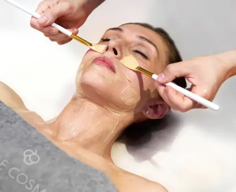 A facial treatment in the spa, in which the hands of a beautician apply a nourishing mask to the face of a relaxed customer with a brush. The customer, with her eyes closed, is visibly enjoying the treatment. The image conveys a feeling of luxury, relaxation and professional skin care.