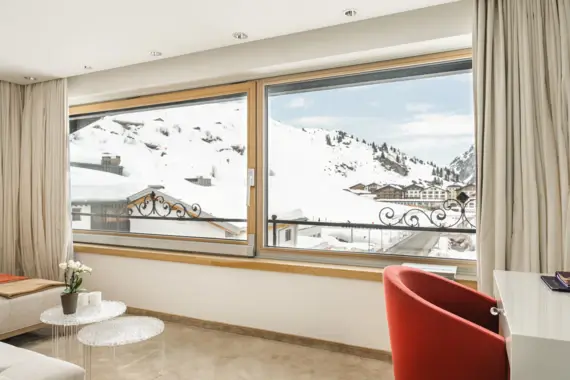 Eim Hotelzimmer mit großen Panoramafenstern durch die man eine verschneite Berglandschaft sieht.