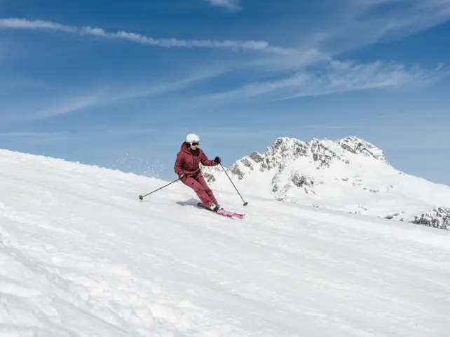 Person beim Skifahren auf einer verschneiten Piste bei blauem Himmel.