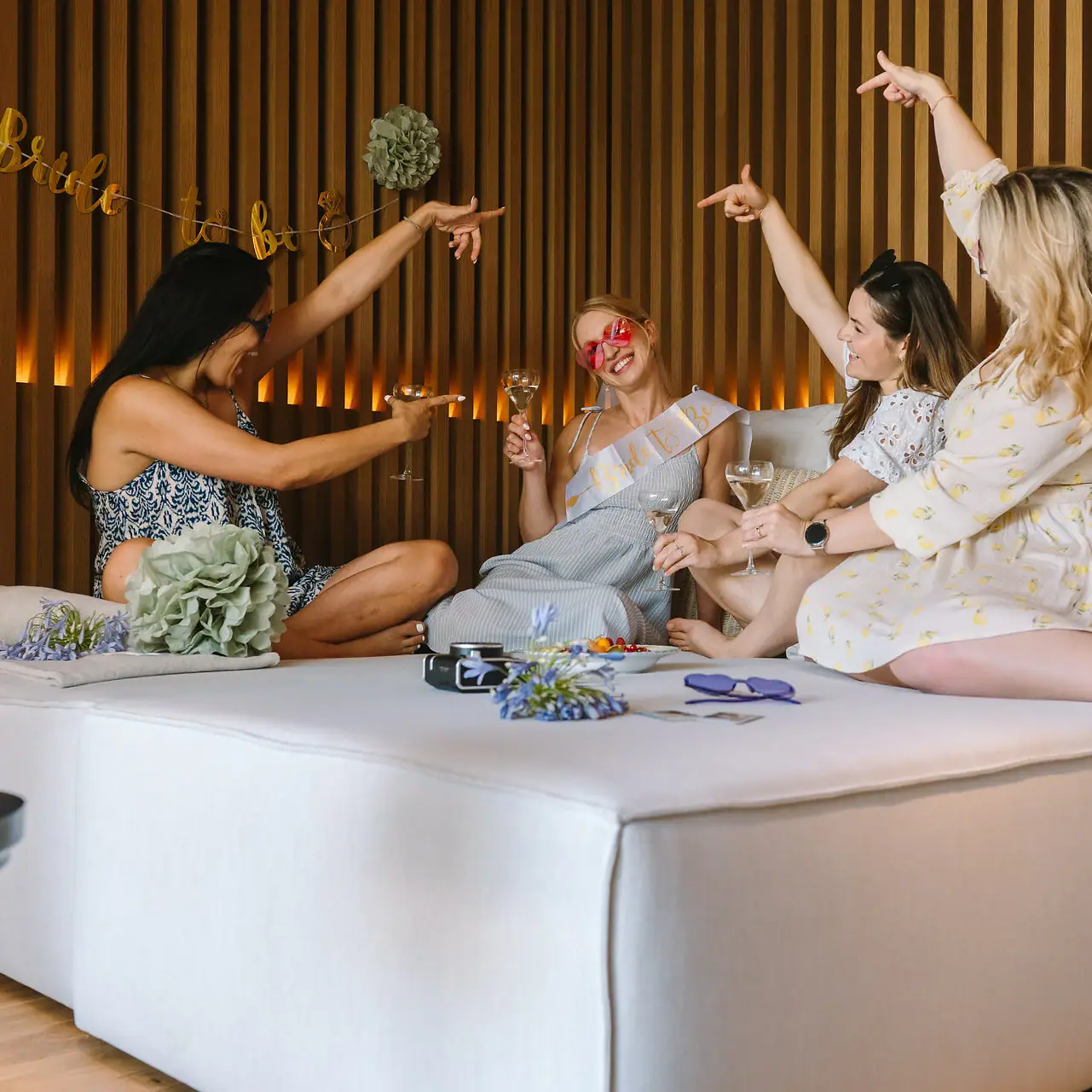 Eine Gruppe von Frauen sitzt mit Getränken auf einem Bett.