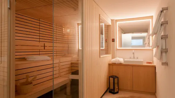 A small sauna area with the entrance to the sauna on the left and a washbasin on the right.