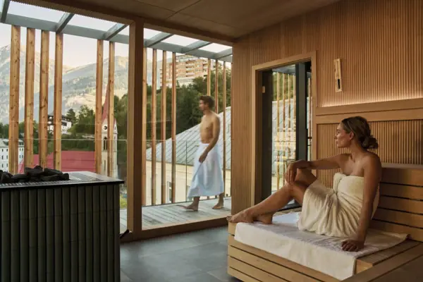Eine Frau sitzt in einer Sauna mit einem Mann im weißen Bademantel.