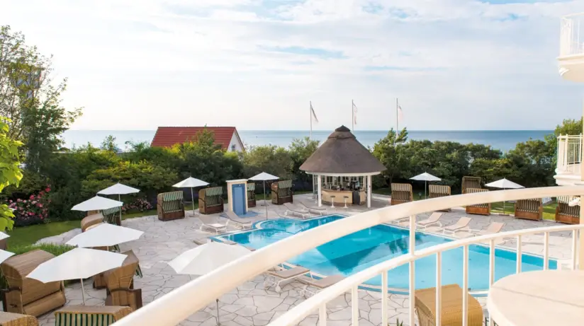 Balkonausblick auf Pool mit Stühlen und Sonnenschirmen am Strand.