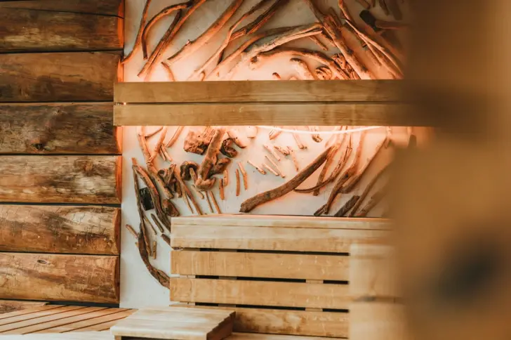 Das Innere einer Sauna, geprägt von einem interessanten Kontrast zwischen rauen, natürlichen Treibholzwänden und den glatten, hellen Holzbänken, die zum Entspannen einladen. Die Wände und die Decke zeigen ein kunstvolles Arrangement von Treibholzstücken.