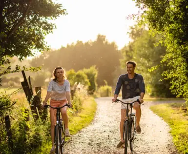 Ein Mann und eine Frau fahren auf einem Weg Fahrrad, umgeben von Bäumen und Gras.