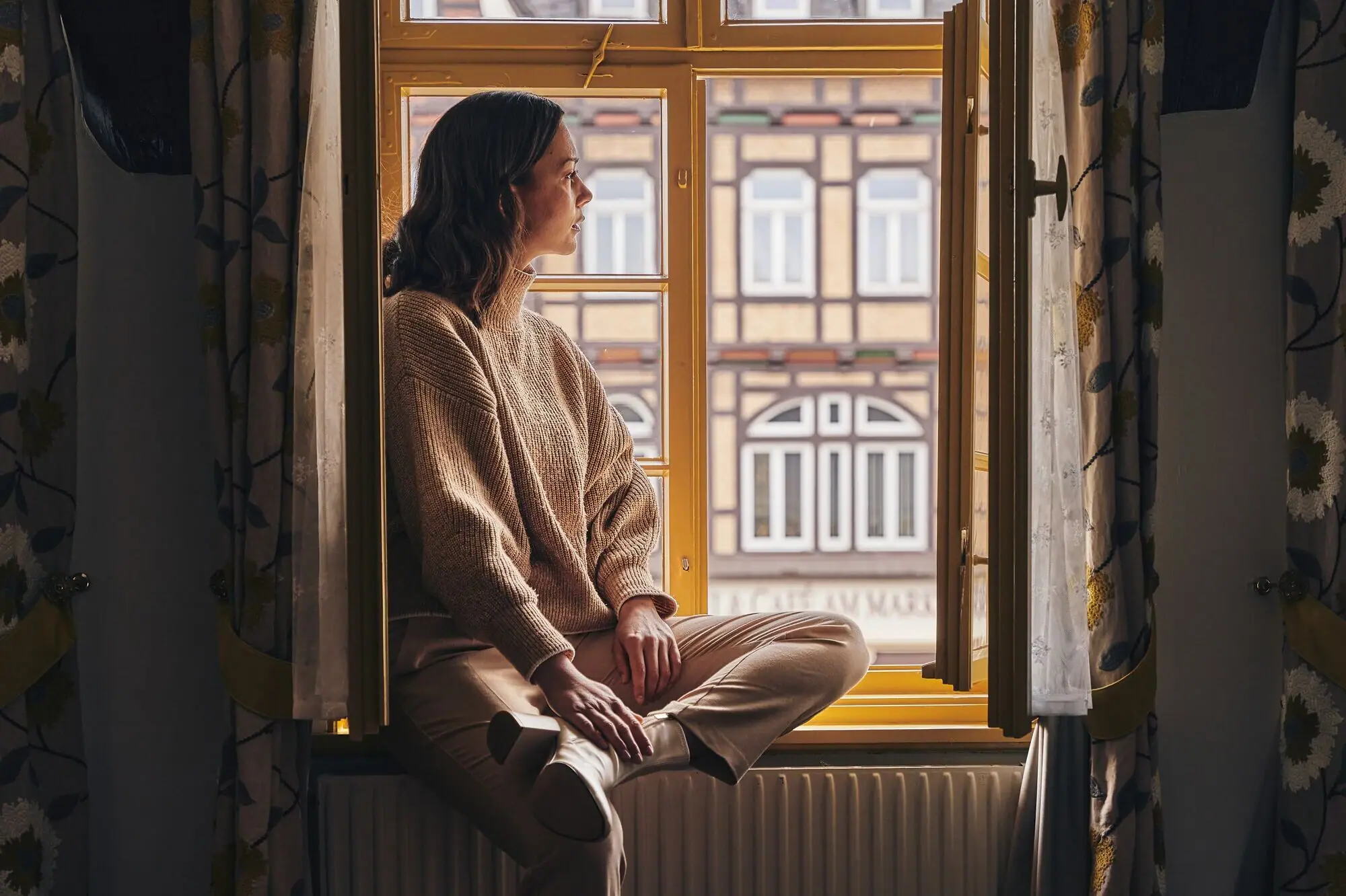 Zimmerausblick Gothisches Haus Eine Frau sitzt auf einer Fensterbank und schaut aus dem Fenster.