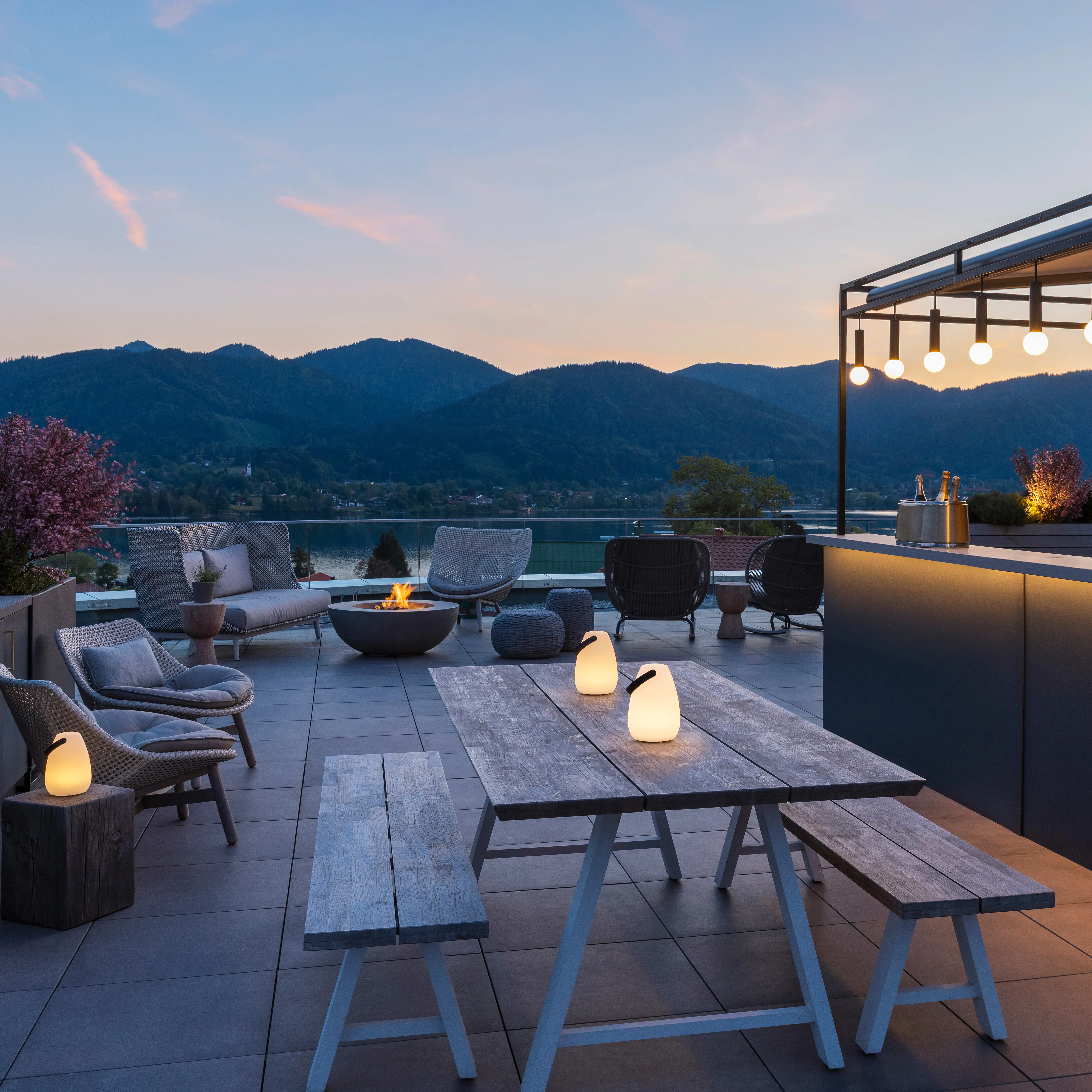 Terrasse mit Tisch und Stühlen, Bar im Hintergrund und Blick auf einen See.