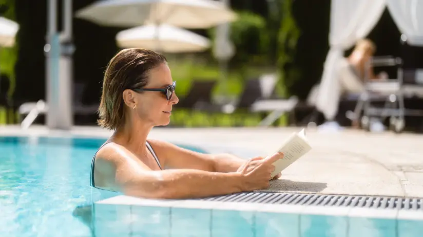 Frau in Badeanzug liest ein Buch im Swimmingpool.