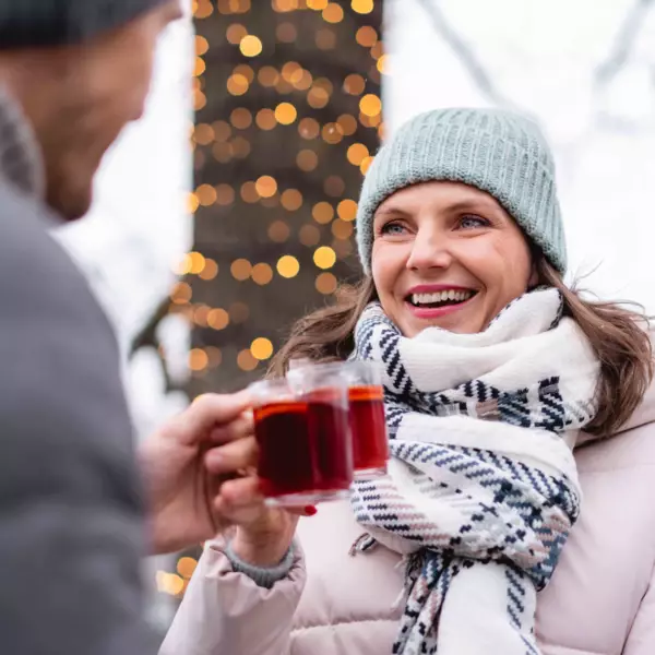 Ein Mann und eine Frau stoßen in winterlicher Umgebung mit rotem Punsch an.