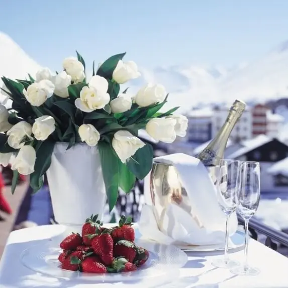 A large bouquet of flowers stands next to a plate of strawberries and a bucket of champagne and two champagne glasses.