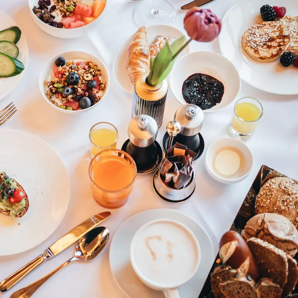 Ein gedeckter Frühstückstisch mit Brotkorb, Pancakes, Saft und Cerealienauswahl
