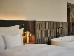 Ein Hotelzimmer, in dem eine frei stehende Badewanne neben einem Bett mit weißer Bettwäsche steht.