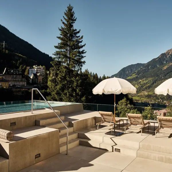 Der Outdoor-Pool im SPA-ROSA Bad Gastein mit Sonnenschirmen und Liegestühlen an einem sonnigen Tag.